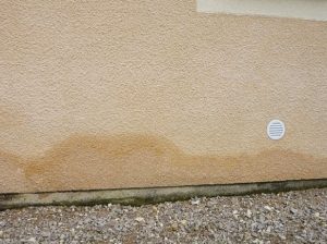 Tache d'humidité sur un mur avec une grille de ventilation.