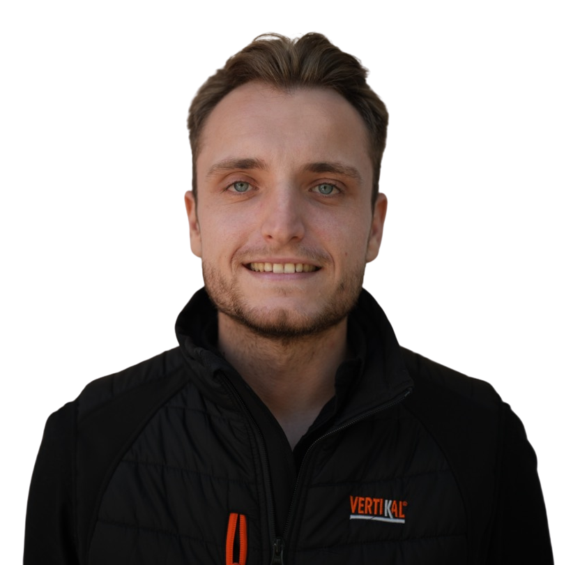 Homme souriant portant une veste noire, façades ariégeoises en arrière-plan.