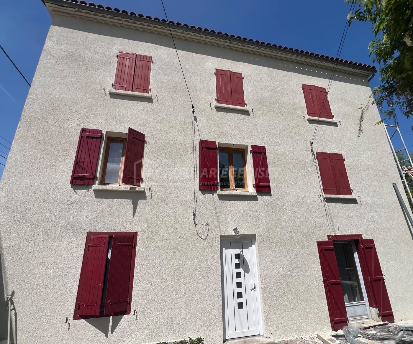 Façade ariégeoise crépie avec volets rouges et porte blanche